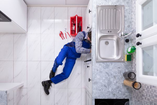 An emergency plumber works beneath a kitchen sink