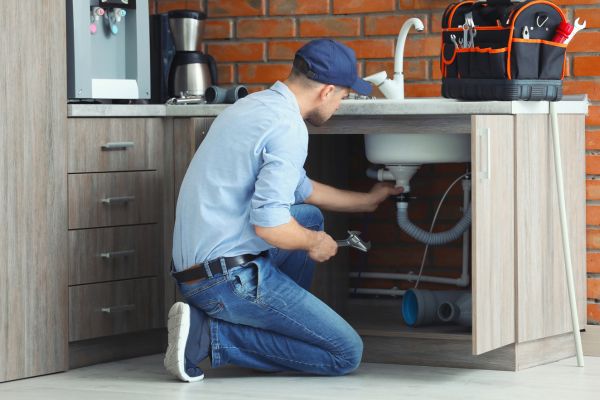 An emergency plumber works beneath a sink