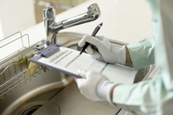 A plumber with a pen and notepad is standing next to a sink. 